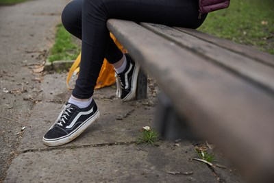 Lower half of a teenager sitting on a park bench
